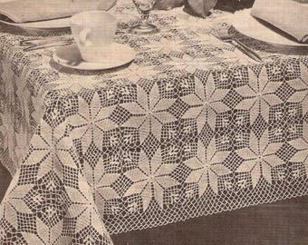 May include: A white crocheted tablecloth with a delicate floral pattern. The tablecloth is laid out on a table with a white cup and saucer, a glass, and a plate with silverware.