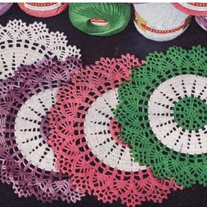 Könnte beinhalten: Vier gehäkelte Deckchen in Weiß, Rosa, Lila und Grün. Die Deckchen sind rund und haben ein zartes Spitzenmuster.