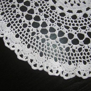 May include: White crocheted doily with a delicate lace pattern. The doily is circular and has a scalloped edge.