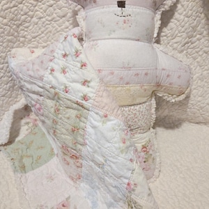 May include: A handmade teddy bear and quilt set. The bear is made of patchwork fabric with floral patterns in pink, white, and light green. The quilt features similar floral patterns and is draped over the bear.