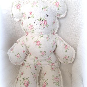 May include: A handmade white teddy bear with a floral pattern of pink roses and green leaves. The bear's face features embroidered eyes and a stitched smile. The bear is approximately 20 inches tall.