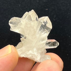 May include: A cluster of clear quartz crystals with a pointed, multi-faceted shape. The crystals are arranged in a cluster, with some of the points facing upwards and others facing downwards.