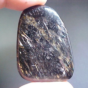 May include: A smooth, black, and gold gemstone with a unique, striated pattern. The stone is polished and has a glossy finish.