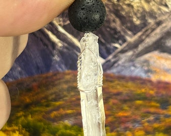 May include: A silver chain necklace with a black lava rock bead and a clear quartz crystal pendant.