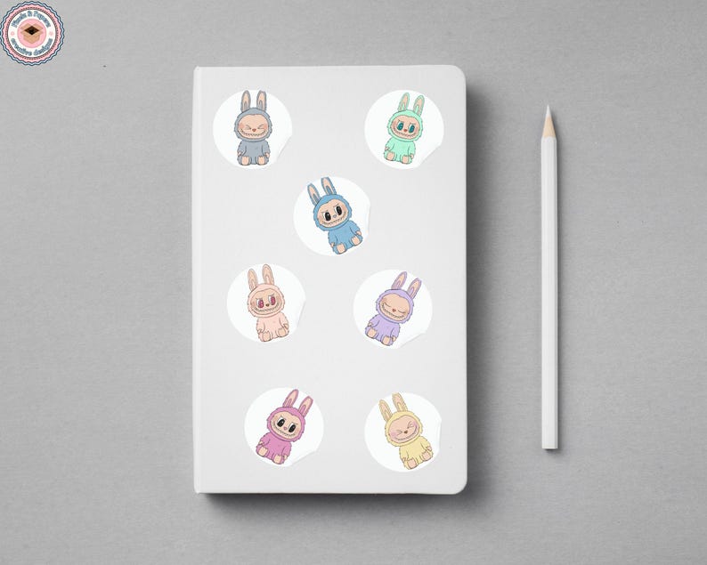 Puede incluir: Un cuaderno blanco con siete pegatinas de conejitos de colores y un l&aacute;piz blanco. Las pegatinas presentan conejitos de dibujos animados en varios colores pastel, incluyendo azul, rosa y amarillo. Las pegatinas est&aacute;n sobre un fondo blanco.