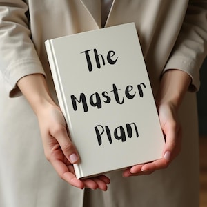 May include: A cream-coloured book with the words "The Master Plan" in black lettering. The book is held by a person wearing a beige jacket.