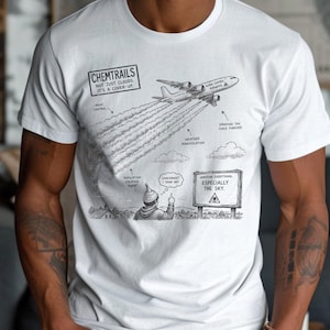 May include: A white t-shirt featuring a black and white graphic illustration of an airplane leaving trails in the sky. The text reads: CHEMTRAILS NOT JUST CLOUDS. IT'S A COVER-UP. MIND CONTROL, WEATHER MANIPULATION, SPRAYING YOU SINCE FOREVER, POPULATION CALMING AGENT, COINCIDENCE? I THINK NOT, QUESTION EVERYTHING. ESPECIALLY THE SKY.