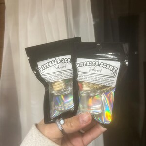 May include: Two Teakwood Diffuser-Scent air fresheners in black packaging. Each has a clear glass bottle with a wooden stopper and a holographic label. The text "DIFFUSER-SCENT Teakwood" is visible on the label.