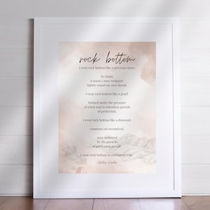Peut inclure: Impression encadrée avec l'inscription "rock bottom" en écriture élégante. L'œuvre présente un fond doux, de style aquarelle, dans des tons roses et beiges. Le poème est centré, chaque ligne de texte est de couleur marron foncé.