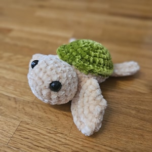 Könnte beinhalten: Eine gehäkelte Plüschschildkröte mit einem beigefarbenen Körper und einer grünen Schale.