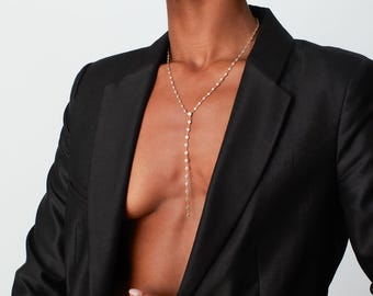 May include: A gold chain necklace with a long pendant and a matching gold chain bracelet with star-shaped charms. The jewelry is worn by a person with dark hair and a black blazer.