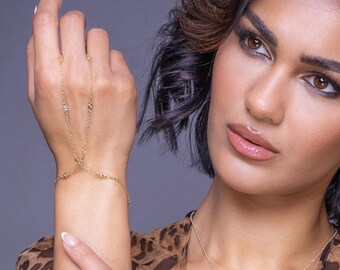 May include: A gold chain bracelet with small clear stones. The bracelet is designed to wrap around the wrist and then extend up to the finger, where it can be worn as a ring.