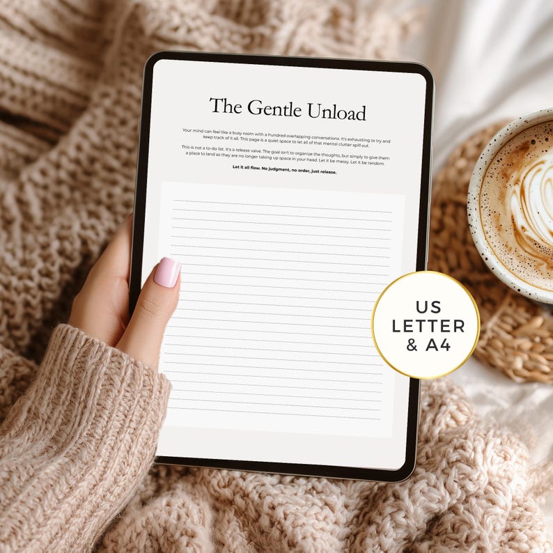 May include: A digital tablet displaying a lined journal page with the title "The Gentle Unload." The tablet is held over a cozy, textured blanket. A coffee cup with latte art sits nearby. The journal is available in US Letter and A4 sizes.