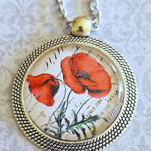 May include: A silver chain necklace with a round pendant featuring a vintage floral design with red poppies on a white background. The pendant has a textured gold rim.