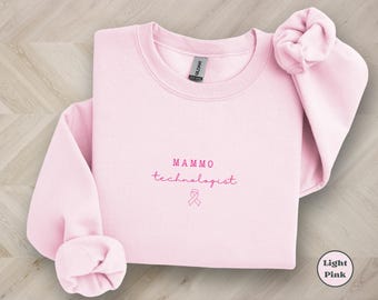 May include: Light pink sweatshirt with the text "MAMMO technologist" and a pink ribbon.