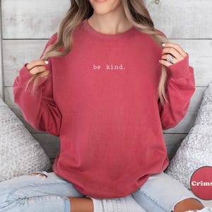 May include: A crimson red sweatshirt with the text "be kind." in white lettering.