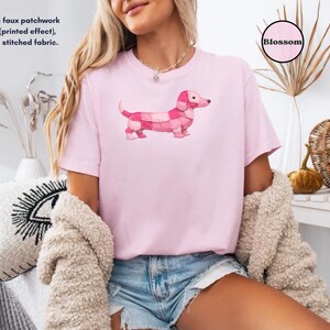 May include: A light pink t-shirt featuring a pink dachshund dog design with a patchwork pattern. The text "Blossom" is in a pink circle. The shirt also has the text: "This is a faux patchwork design (printed effect), not real stitched fabric."