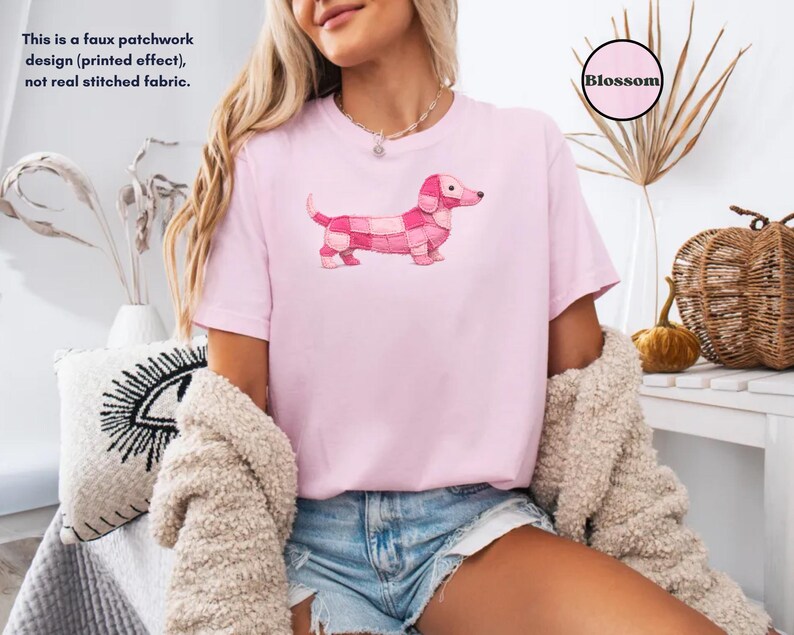 May include: A light pink t-shirt featuring a pink dachshund dog design with a patchwork pattern. The text "Blossom" is in a pink circle. The shirt also has the text: "This is a faux patchwork design (printed effect), not real stitched fabric."
