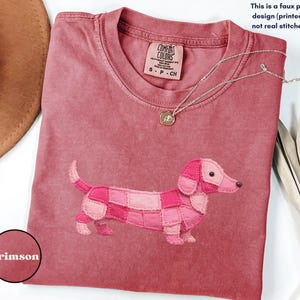 May include: Crimson-colored t-shirt featuring a patchwork dachshund design. The shirt has a crew neck and short sleeves. The text on the shirt reads "COMFORT COLORS" and "S-P-CH". The image also includes the text "This is a faux patchwork design (printed effect), not real stitched fabric."
