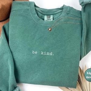May include: A light green sweatshirt with the text "be kind." printed on the front.