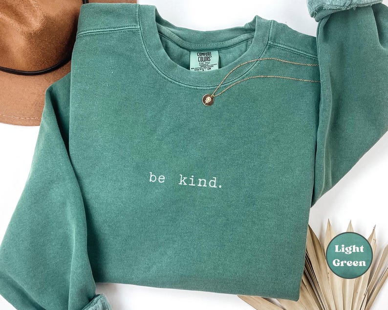 May include: A light green sweatshirt with the text "be kind." printed on the front.