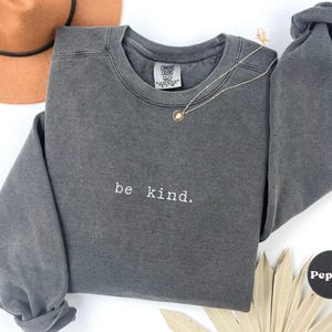 May include: A dark gray sweatshirt with the text "be kind." printed in white on the front.