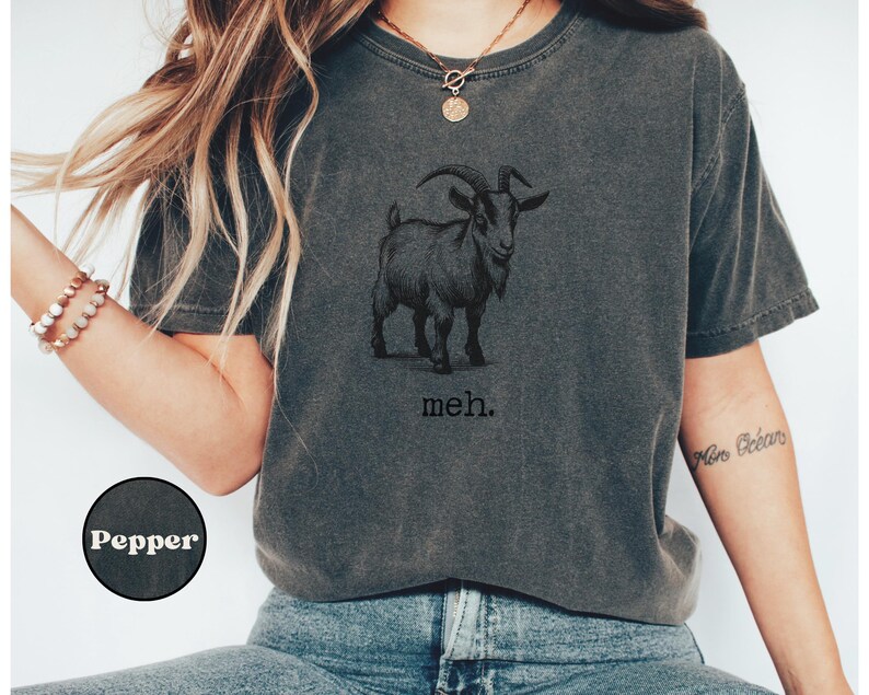 May include: A dark gray t-shirt with a black and white illustration of a goat and the text "meh."
