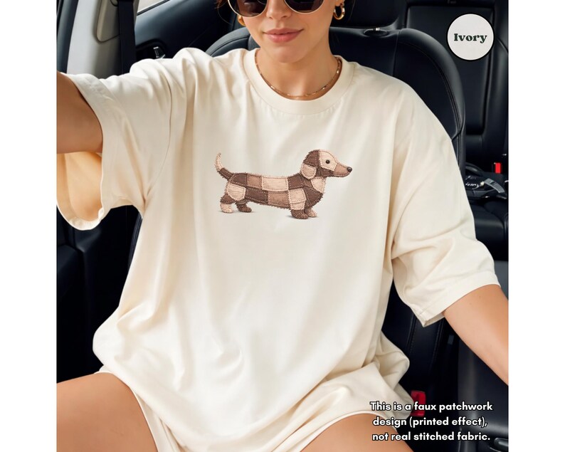 May include: Ivory-colored t-shirt featuring a dachshund dog illustration with a patchwork design. The dog is depicted in shades of brown and tan. The text on the shirt reads: "This is a faux patchwork design (printed effect), not real stitched fabric."