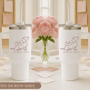 May include: Two white insulated tumblers with handles, each featuring a dachshund illustration and the name "Charlie." The text "Life's Better with a Dachshund" is below the dog. Each tumbler has a silver lid and a straw.