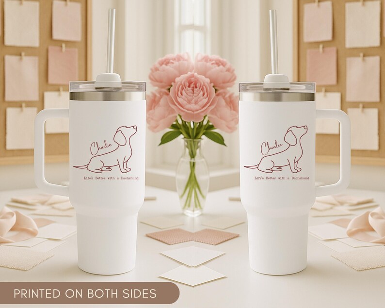 May include: Two white insulated tumblers with handles, each featuring a dachshund illustration and the name "Charlie." The text "Life's Better with a Dachshund" is below the dog. Each tumbler has a silver lid and a straw.