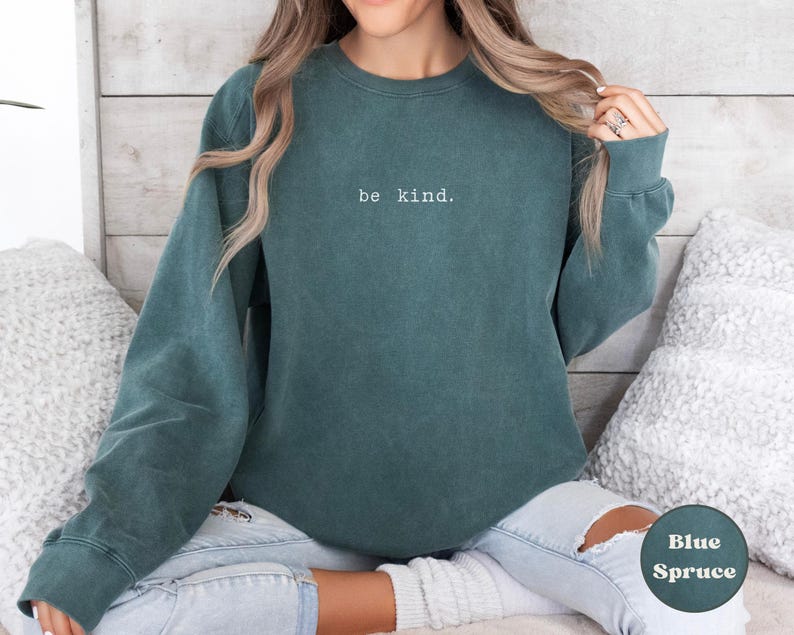 May include: A teal blue sweatshirt with the text "be kind." printed in white on the front.