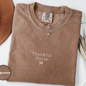 May include: Espresso brown t-shirt with the text "Thankful Nurse." and a small bandage graphic.