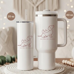 May include: Two white insulated tumblers, one 20 oz and one 40 oz, with a dachshund outline and the name "Charlie" in a script font. The text "Life's better with a dachshund" is below the dog illustration. Both tumblers have a straw.