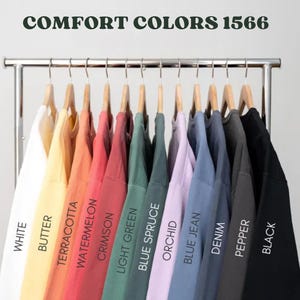 May include: A rack of 12 different colored sweatshirts, labeled with the names of the colors: White, Butter, Terracotta, Watermelon, Crimson, Light Green, Blue Spruce, Orchid, Blue Jean, Denim, Pepper, and Black. The rack is labeled "COMFORT COLORS 1566".