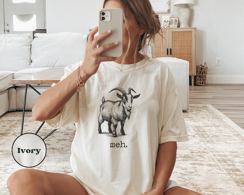 May include: A white t-shirt with a black and white illustration of a goat and the text "meh."