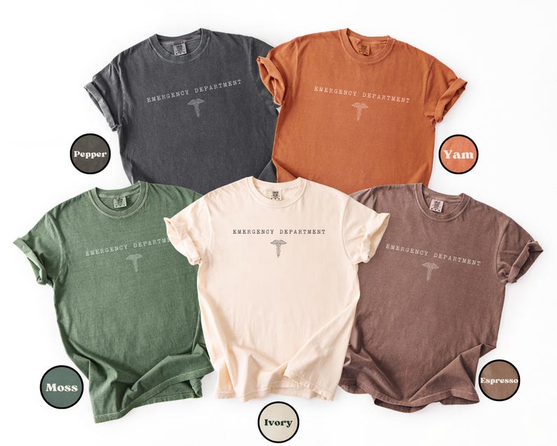 May include: Five short-sleeve crew neck t-shirts in pepper, yam, moss, ivory, and espresso colors. Each shirt features the text EMERGENCY DEPARTMENT printed in a simple font above a caduceus symbol centered on the chest area of the garment.