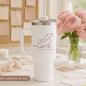 May include: White 40 oz custom tumbler with a handle, featuring a dachshund illustration and the name "Charlie". The text "Life's better with a Dachshund" is below the dog. A straw and lid are included.