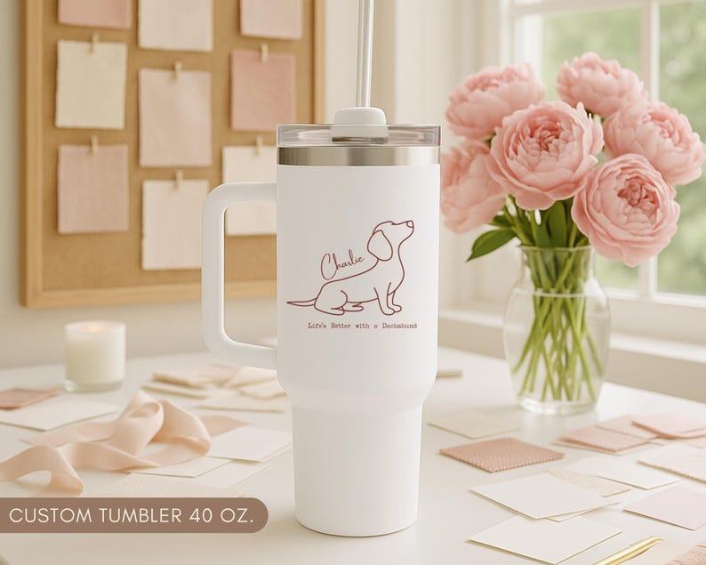 May include: White 40 oz custom tumbler with a handle, featuring a dachshund illustration and the name "Charlie". The text "Life's better with a Dachshund" is below the dog. A straw and lid are included.