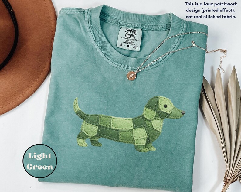 May include: A light green Comfort Colors t-shirt featuring a patchwork dachshund design in shades of green. The shirt has a crew neck and short sleeves. The text "Light Green" is in a circle on the bottom left.