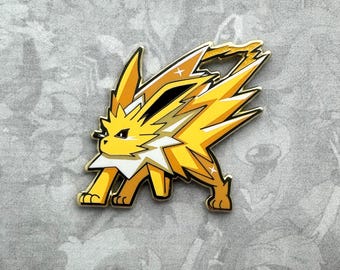 May include: A gold-colored enamel pin featuring a cartoon depiction of the Pokemon Jolteon. The Pokemon is standing on all fours with its tail raised in the air. The pin has a shiny, metallic finish.