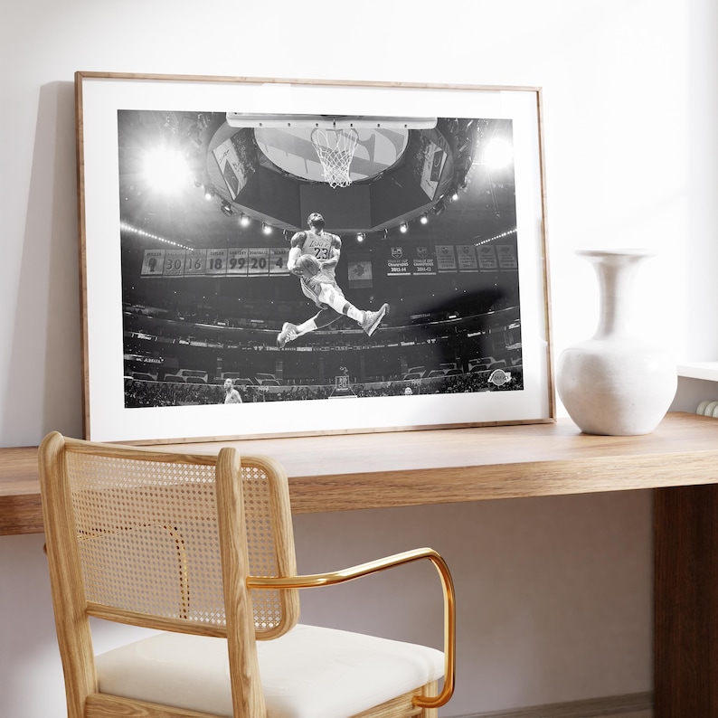 Puede incluir: Fotograf&iacute;a en blanco y negro de un jugador de baloncesto en el aire, a punto de hacer un mate. El jugador lleva una camiseta con el n&uacute;mero "23". La fotograf&iacute;a est&aacute; enmarcada y colgada en una pared.