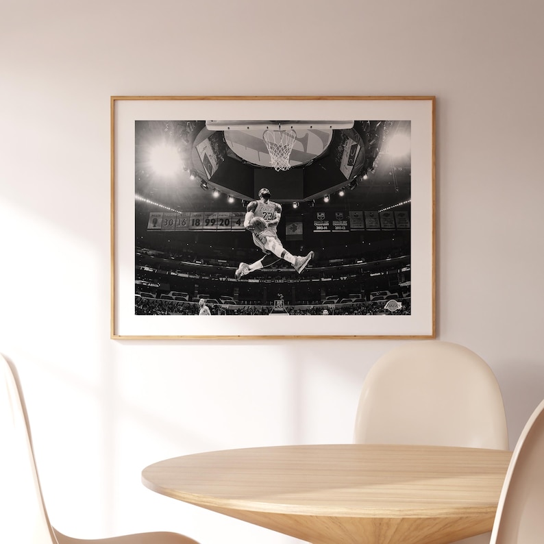 Puede incluir: Fotograf&iacute;a en blanco y negro de un jugador de baloncesto en el aire, a punto de hacer un mate. El jugador lleva una camiseta con el n&uacute;mero 23. La foto fue tomada en un estadio con una multitud de personas en el fondo.