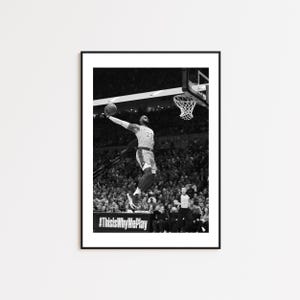 Könnte beinhalten: Schwarz-Weiß-Druck in einem Rahmen, der einen Basketballspieler in der Luft zeigt, kurz davor, den Ball zu dunken. Der Spieler trägt ein Trikot mit der Nummer 23. Der Text "#ThisIsWhyWePlay" ist unten im Bild zu sehen.