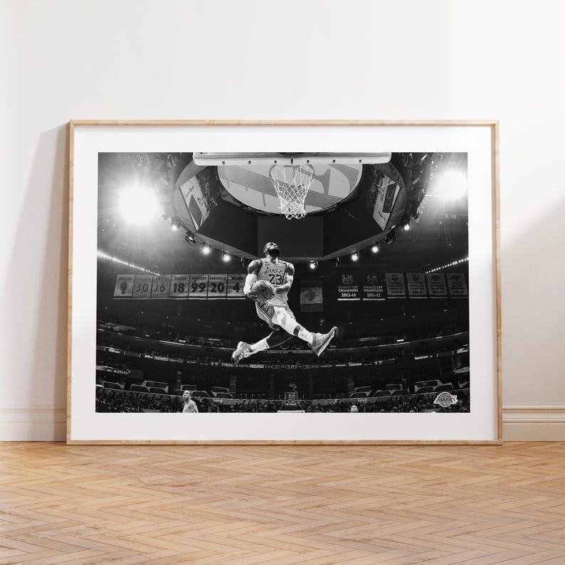 Puede incluir: Fotograf&iacute;a en blanco y negro de un jugador de baloncesto en el aire, a punto de hacer un mate. El jugador lleva una camiseta con el n&uacute;mero "23". La foto fue tomada en un estadio con una gran multitud de fondo.