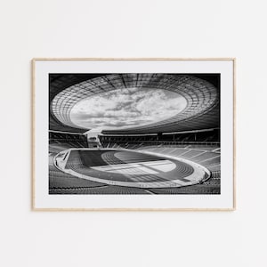 Könnte beinhalten: Schwarz-Weiß-Fotografie eines Stadioninnenraums. Das Bild zeigt eine Laufbahn, Sitzreihen und eine große Öffnung in der Decke. Das Stadion hat ein modernes, kreisförmiges Design mit einem teilweise offenen Dach.