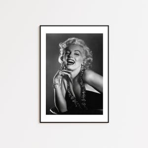 May include: Black and white portrait photograph of a woman with blonde hair laughing. She is wearing a low-cut black dress and a necklace with large stones.