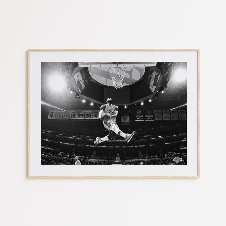 Puede incluir: Fotograf&iacute;a en blanco y negro de un jugador de baloncesto en el aire, a punto de hacer un mate. El jugador lleva una camiseta con el n&uacute;mero 23. La foto fue tomada en un estadio con una multitud de fondo.