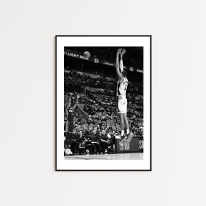 May include: Black and white framed print of a basketball player mid-air, shooting a ball. The player is wearing a jersey with the number 7. The background shows a crowd of spectators and the words "LIGHT BEER".
