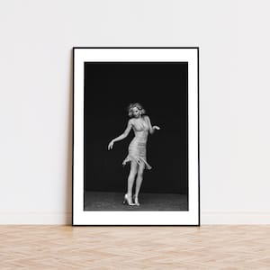 May include: A black and white photograph of a woman wearing a sequined dress and heels, posing against a dark backdrop.