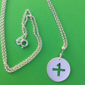 May include: A silver chain necklace with a round pendant featuring a cut-out cross design.